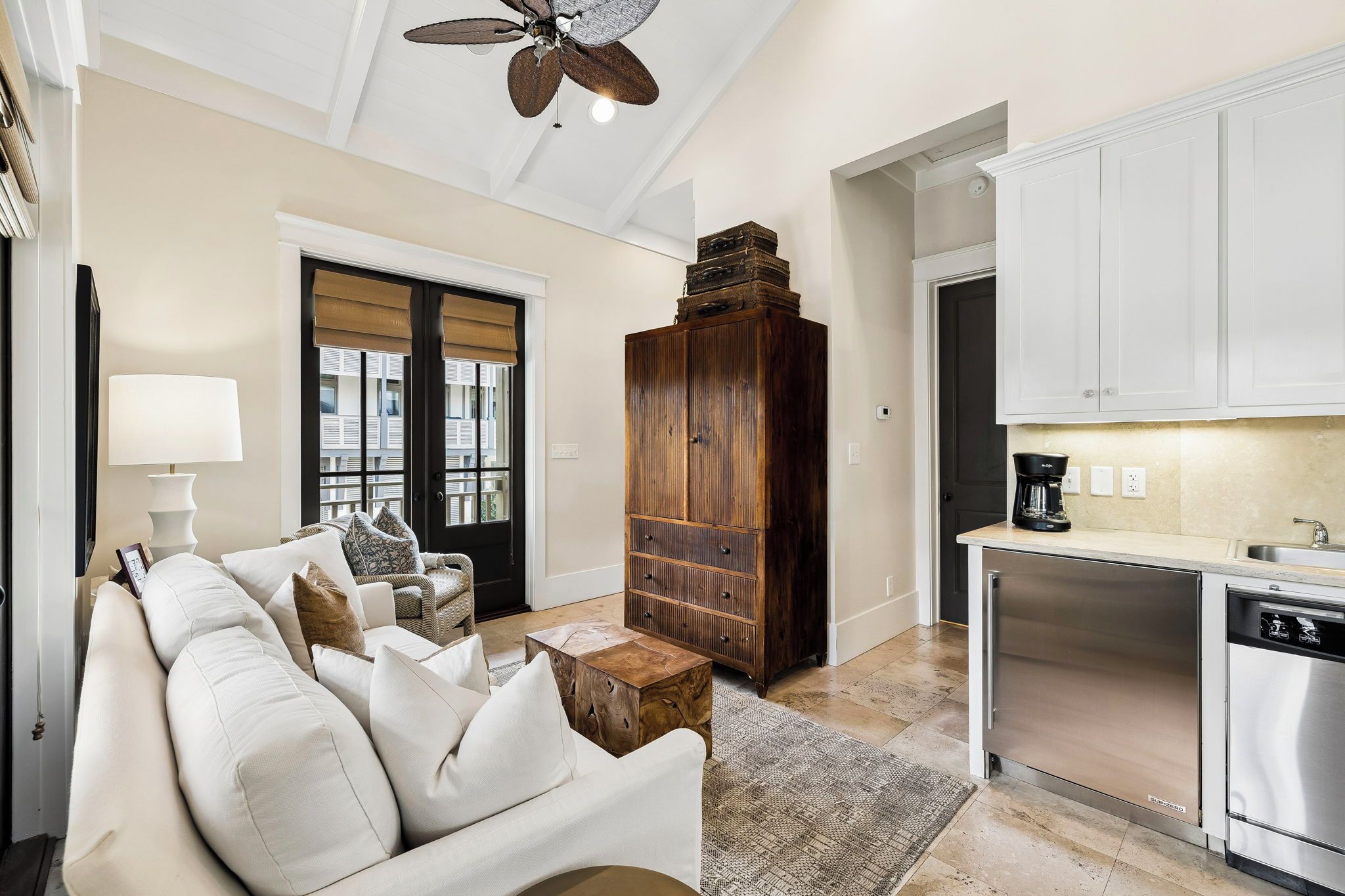 A living room with a sofa, coffee table, and a wooden cabinet. There is a kitchen area with a dishwasher and cabinets.