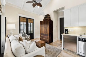 A living room with a sofa, coffee table, and a wooden cabinet. There is a kitchen area with a dishwasher and cabinets.