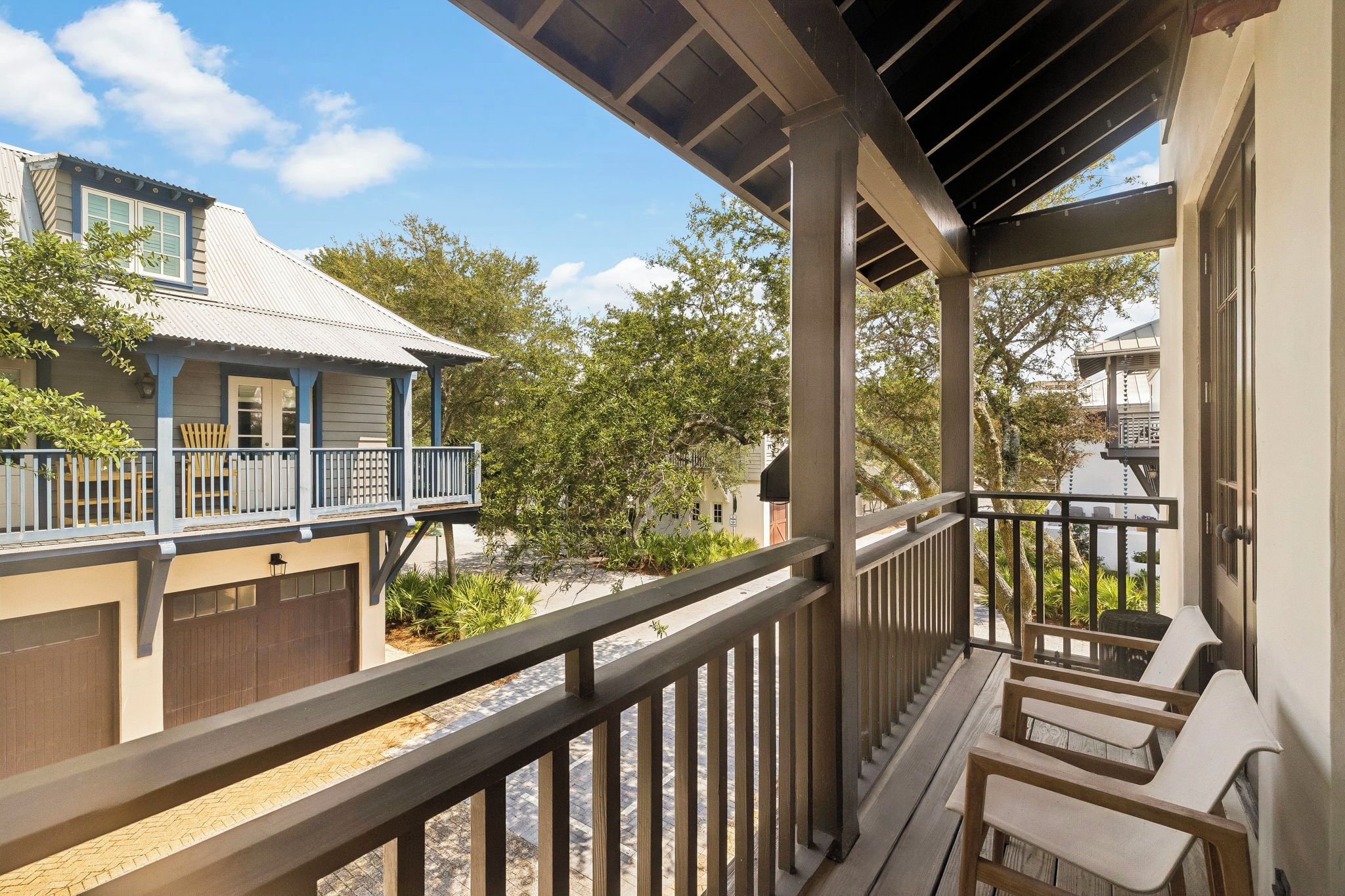 Un balcon couvert avec des balustrades en bois, une vue sur un immeuble avec un garage, et un arbre en arrière-plan.