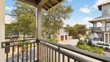 A balcony with a view of a residential area, including a house with a garage and a tree-lined street.