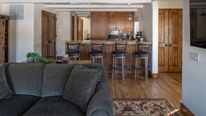 Una cocina moderna con armarios de madera, una isla central con taburetes y un sofá gris en la sala de estar.
