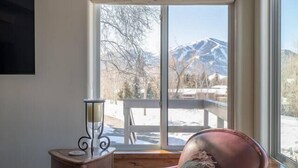 Una habitación con una butaca de cuero, una mesita con una vela y vistas a montañas a través de amplios ventanales.