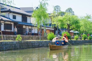 A traditional boat with passengers, a stone wall, and buildings with tiled roofs. - Okayama Green Hotel (Okayama)