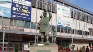 A statue in front of a building with large advertisements. - Okayama Green Hotel (Okayama)