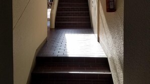 Un escalier étroit, avec un extincteur fixé au mur, mène à une pièce dotée d’une fenêtre.