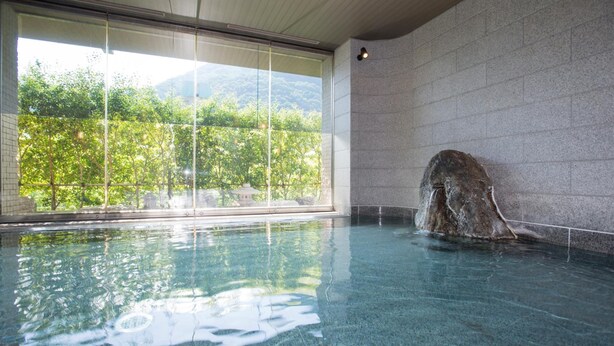 An indoor swimming pool with clear glass walls, a stone feature, and a view of greenery outside. - Kinu No Keikoku Hekiryu (Nikko)