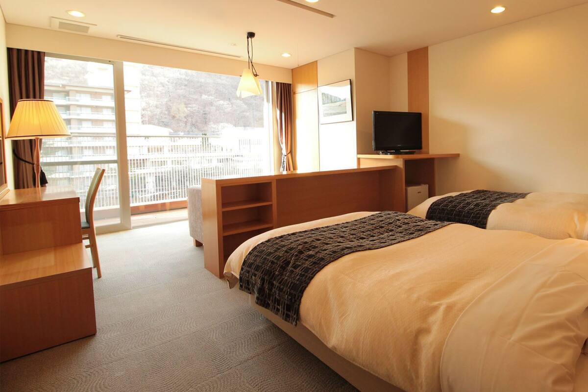 Een hotelkamer met een bed, bureau, televisie en uitzicht op een balkon.