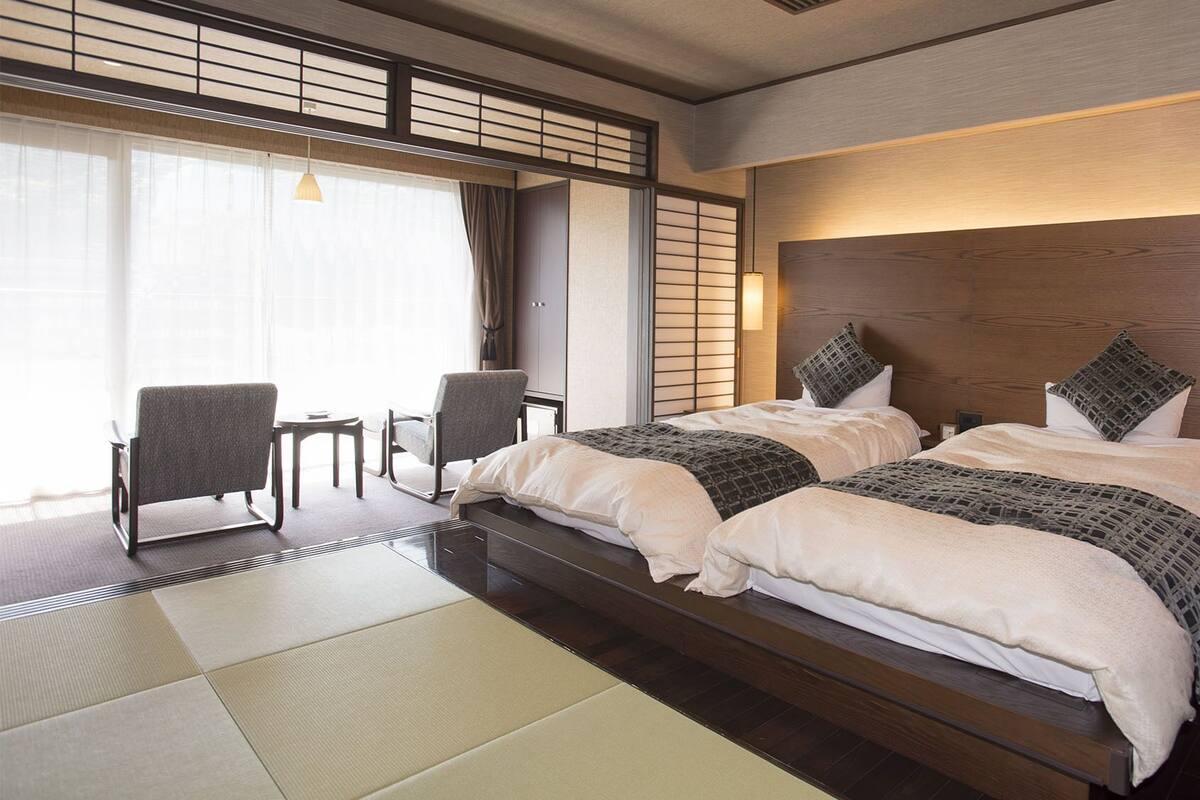 Een hotelkamer met een groot bed, twee stoelen, een tafeltje en uitzicht op de omgeving.