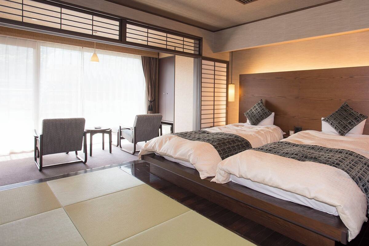 Een hotelkamer met een groot bed, twee stoelen, een klein tafeltje en uitzicht op buiten.