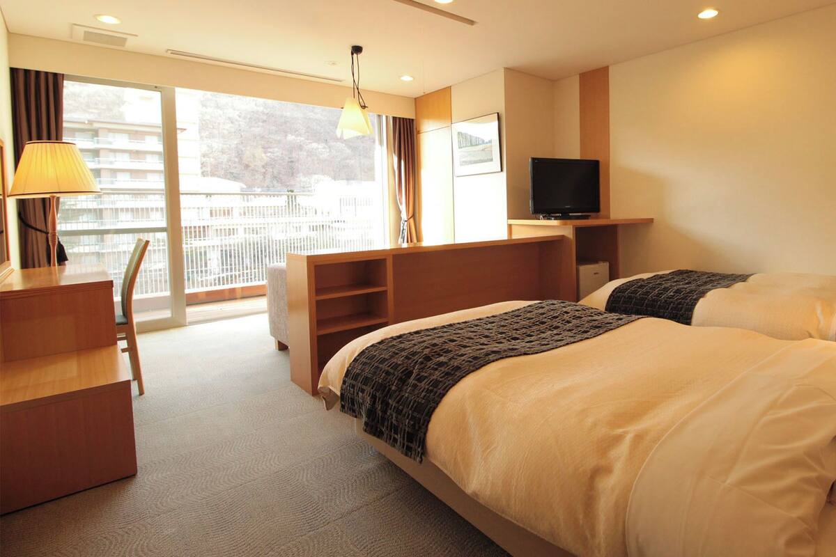 Een hotelkamer met twee bedden, een bureau, een televisie en een balkon met uitzicht.
