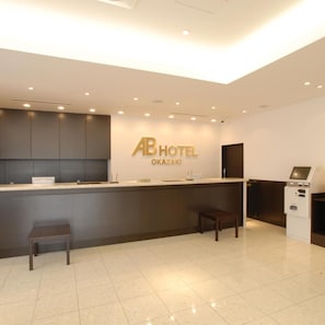 Un'area reception di un hotel dal design moderno, con scrivania, angolo salotto e un chiosco self-service.