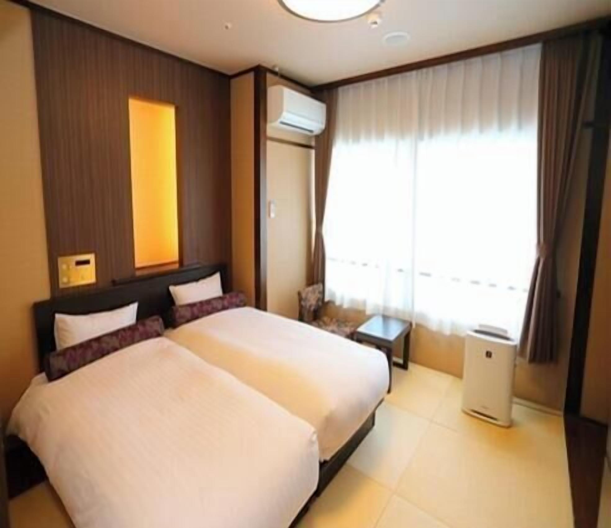 Habitación de hotel con dos camas, una mesita, un equipo de aire acondicionado y una ventana con cortinas.