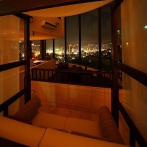 A room with a large window overlooking a cityscape at night.