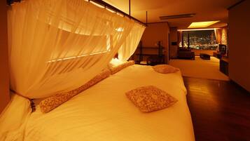 A bedroom with a canopy bed, a view of the city at night, and a seating area with a TV.