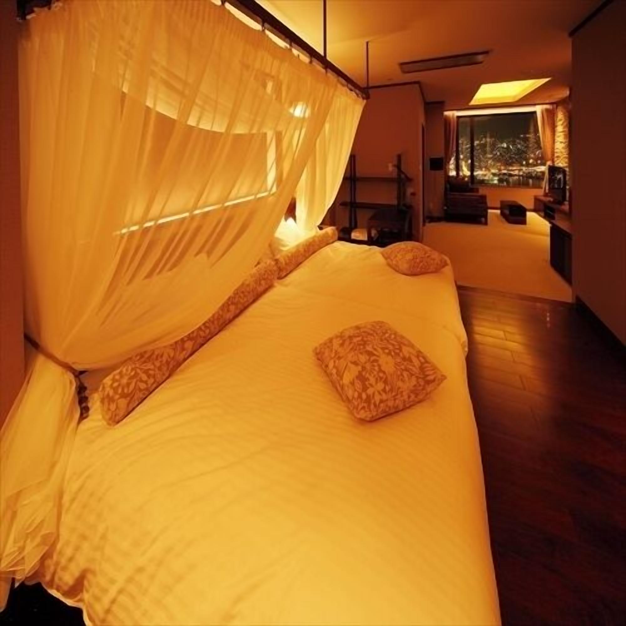 Una cama con dosel, una mesita de noche y vista a la ciudad a través de una ventana.