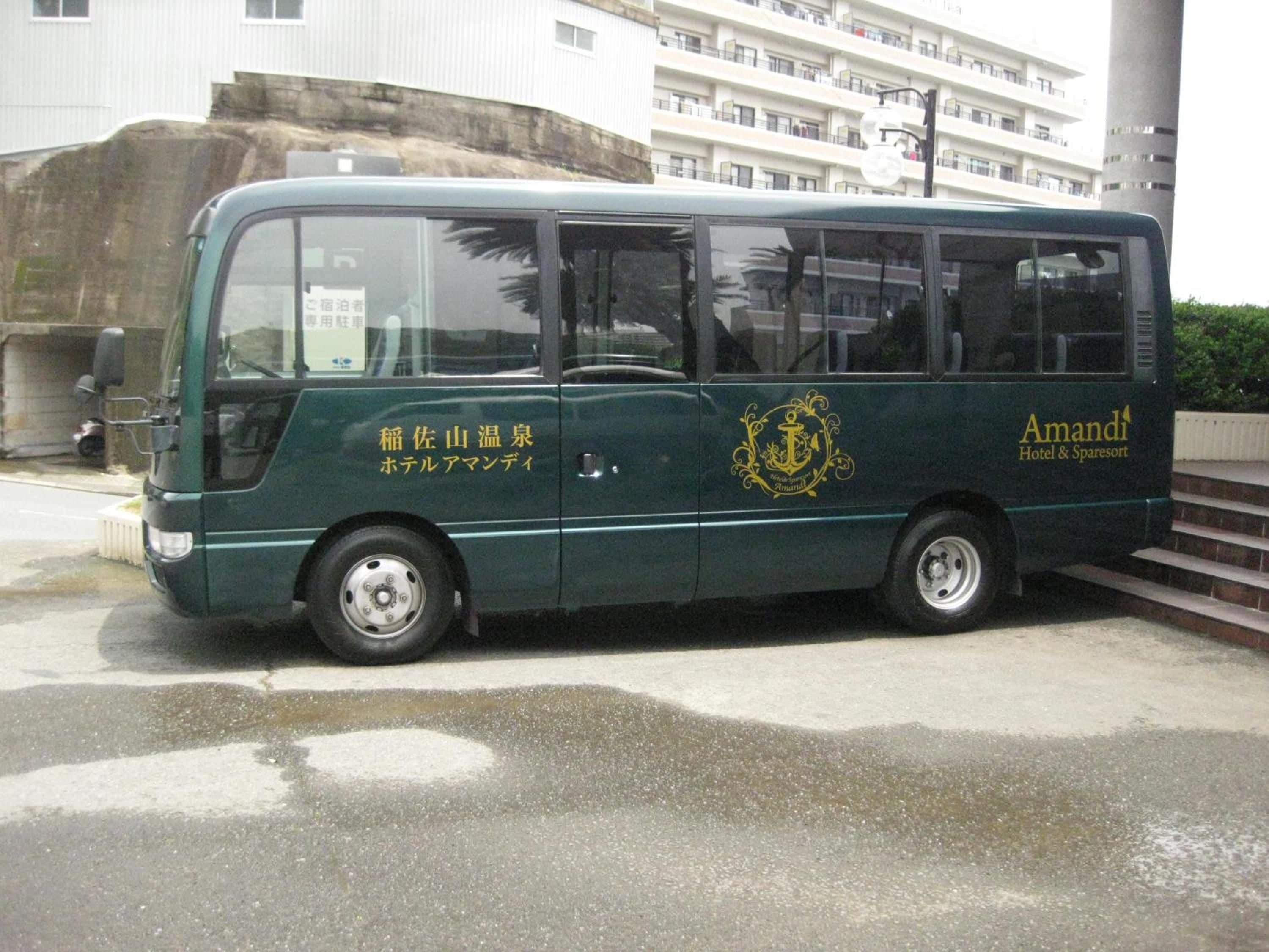 A green bus with 'Amandi Hotel & Sparesort' branding, parked on a wet road with a building in the background.