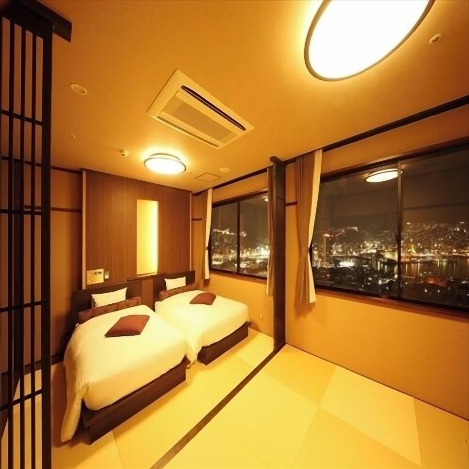 Habitación de hotel con dos camas, un ventanal con vistas a la ciudad y una puerta corredera tradicional japonesa.