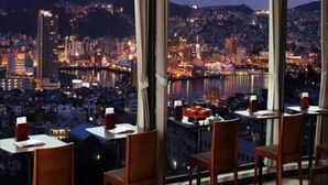 Un espace repas doté de grandes fenêtres donnant sur une vue panoramique de la ville la nuit.