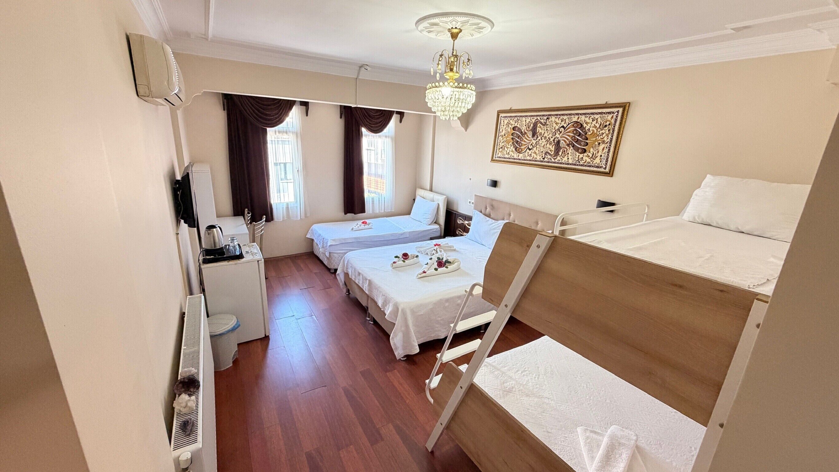 A hotel room with two single beds, a desk with a kettle, a chair, a small table, and a decorative wall piece.