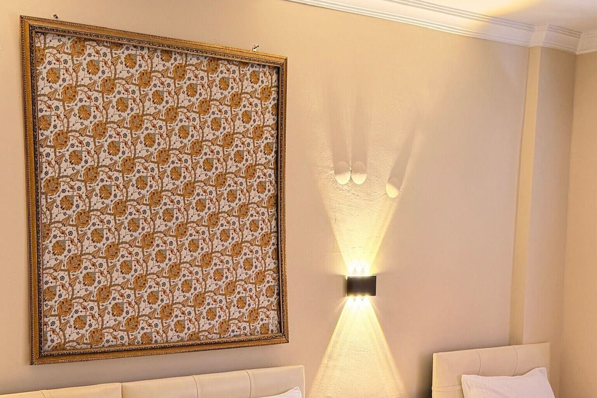 A hotel room with a large bed, two bedside tables, a wall-mounted lamp, and a decorative wall hanging.