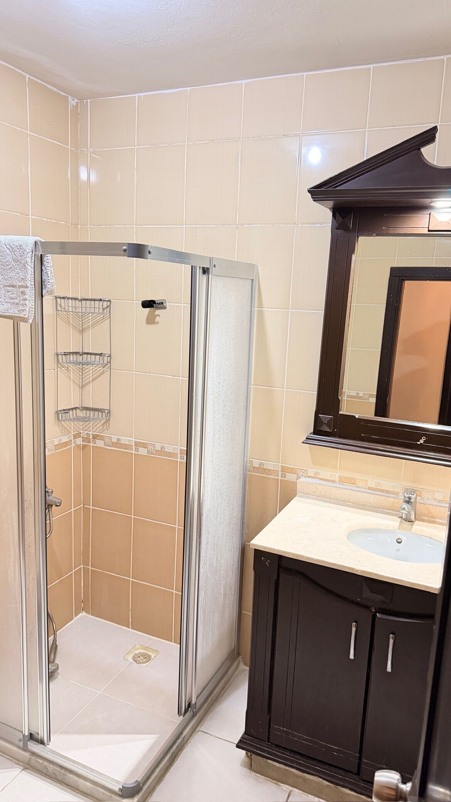 A bathroom with a glass-enclosed shower, a sink with a mirror above it, and a tiled floor.
