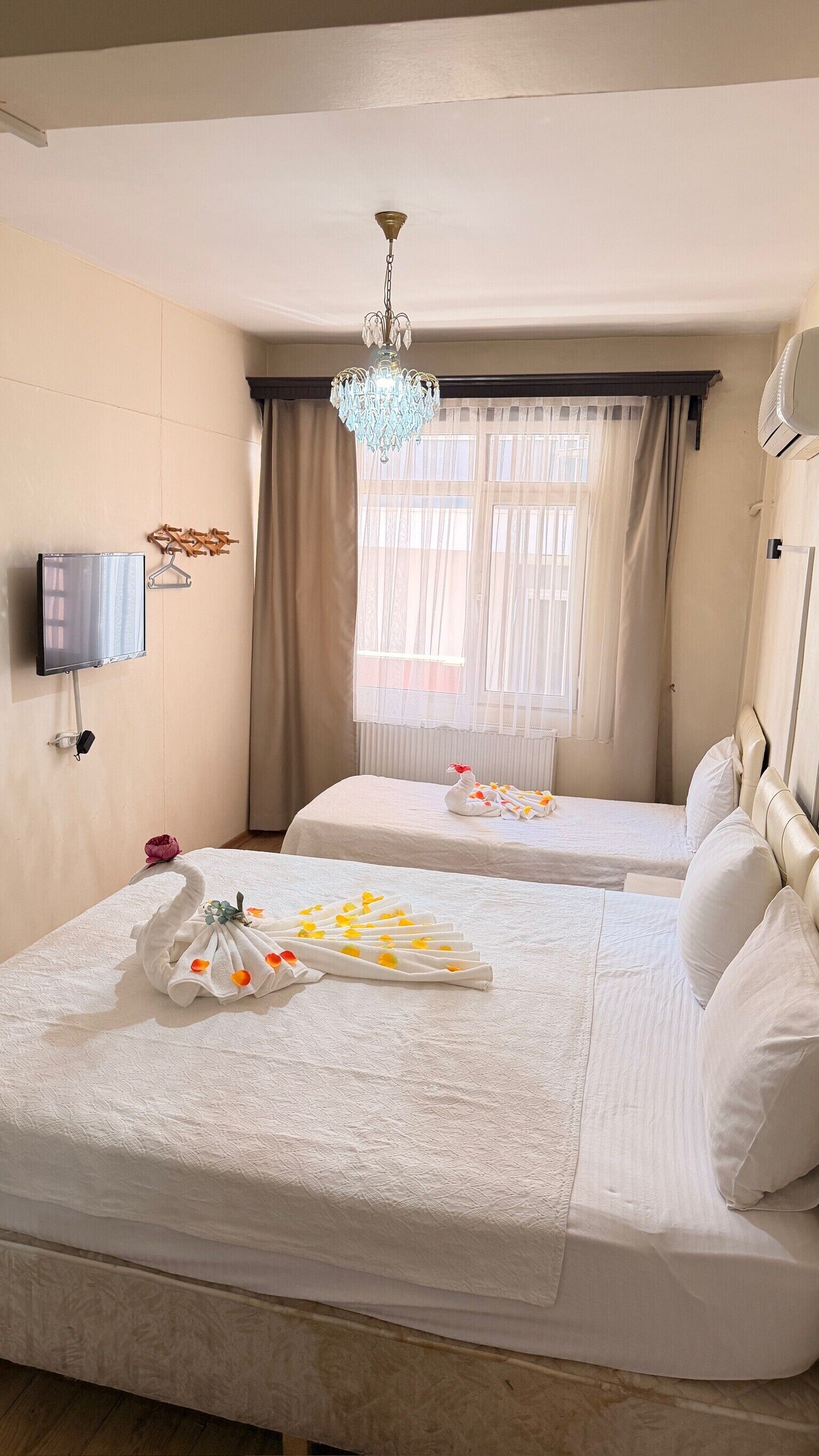 A hotel room with two beds, a chandelier, a TV, and a window with curtains.
