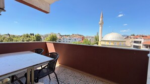 Un balcon avec une table et des chaises, donnant sur un paysage urbain où l’on aperçoit une mosquée et des immeubles.