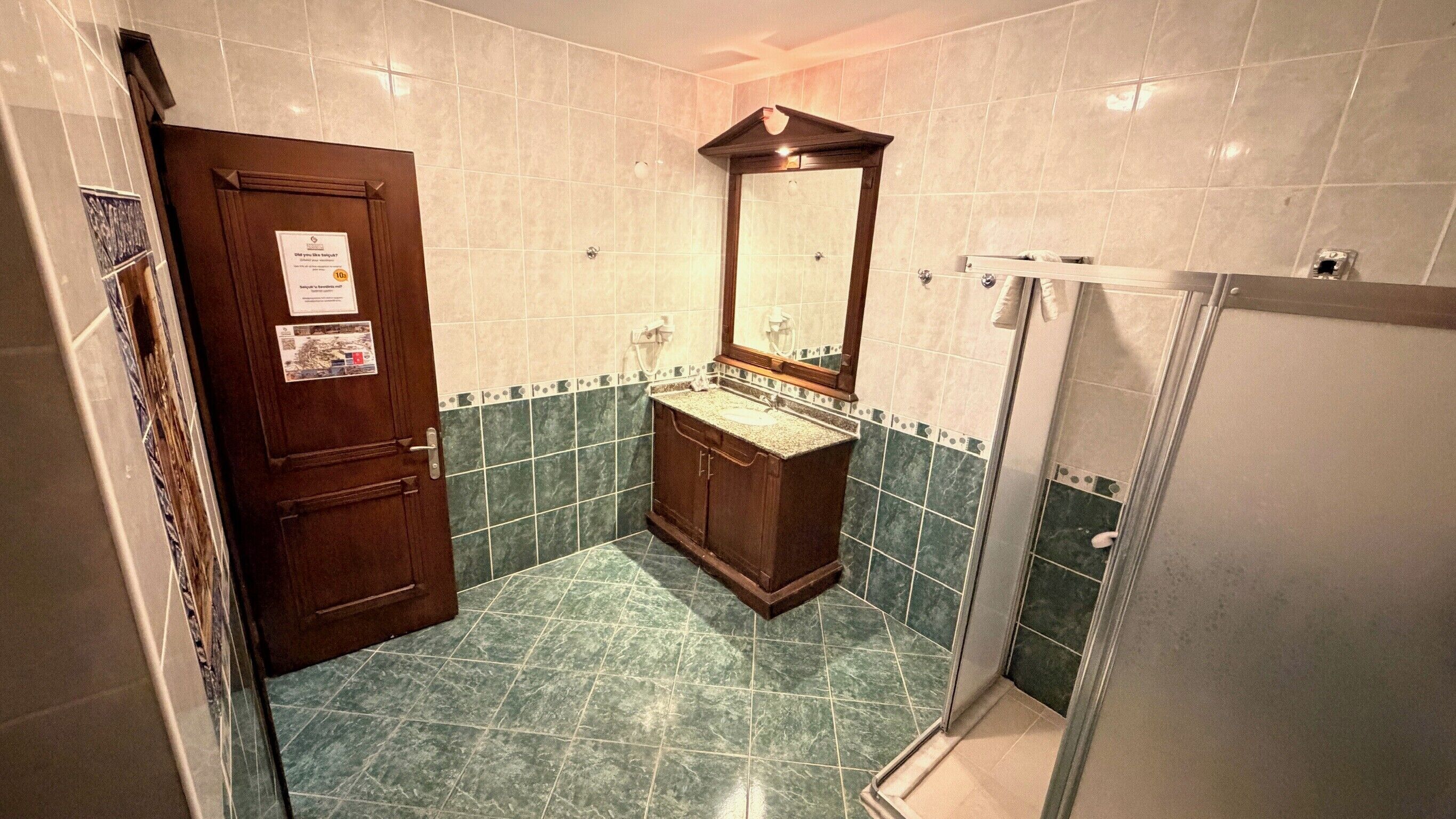 A bathroom with a wooden door, a sink with a mirror, and a shower area.