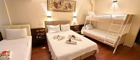 Une chambre d’hôtel avec deux lits simples, un lit double et un lit superposé. On y trouve des coussins décoratifs, un lustre et une œuvre d’art murale.