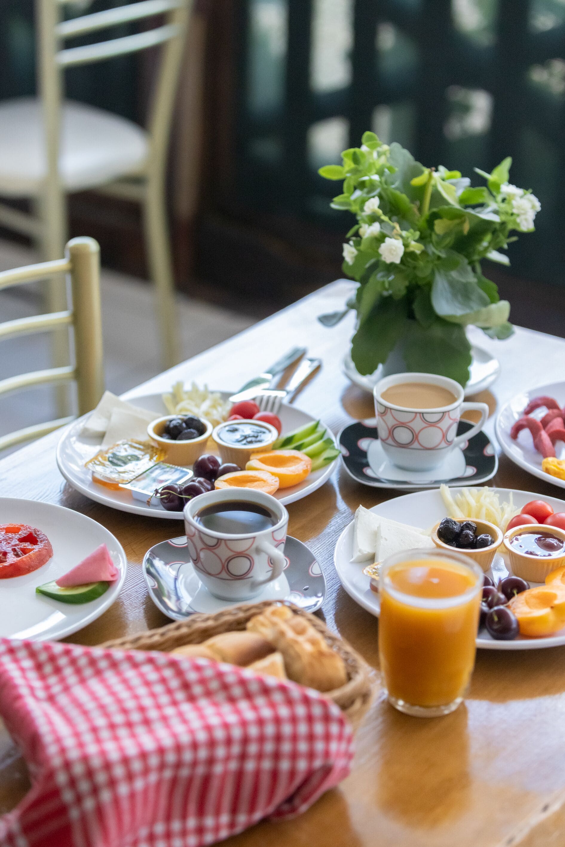 A breakfast table with plates of food, cups of coffee, and a vase of flowers.
