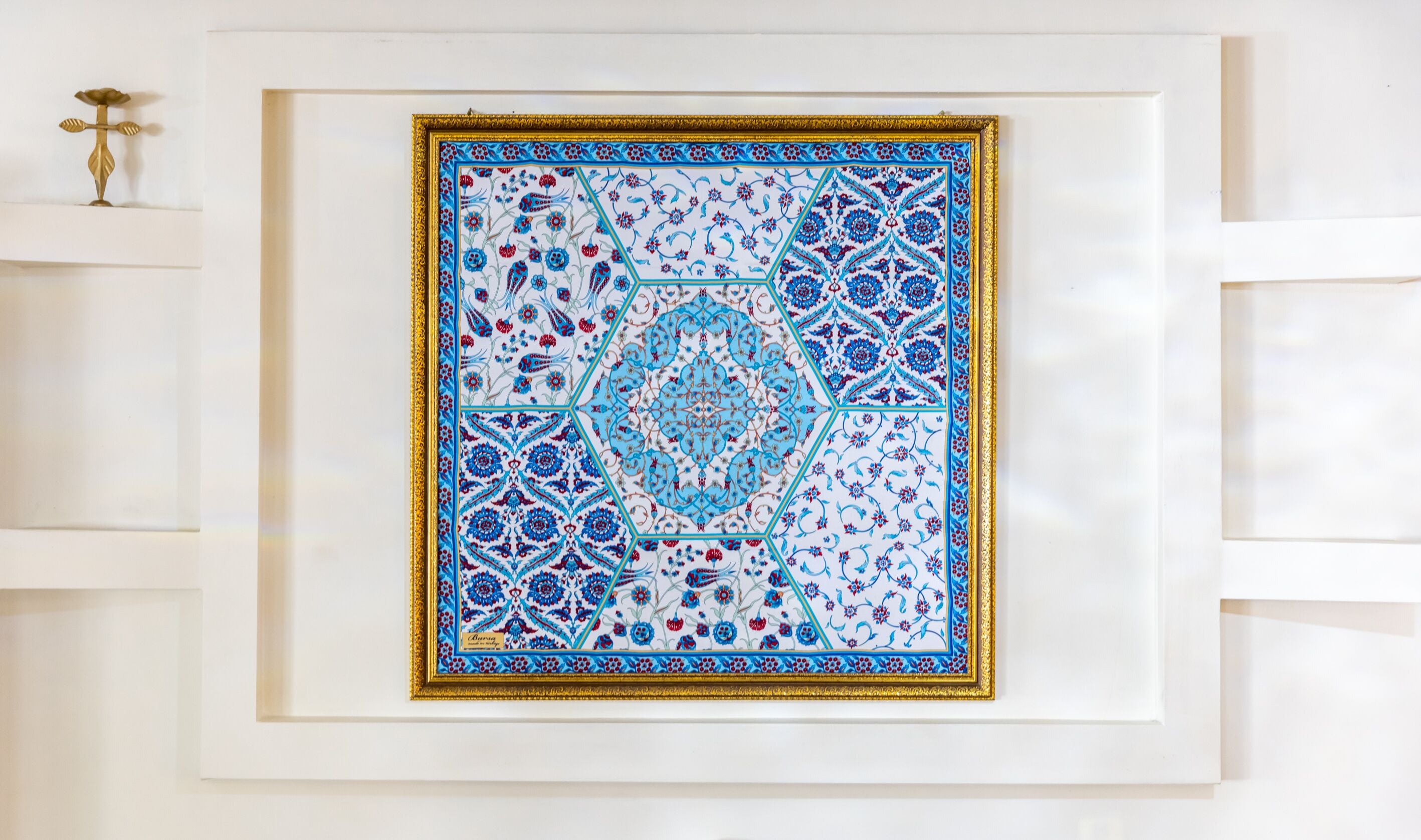 A framed artwork with intricate blue and red floral patterns, displayed on a white wall.