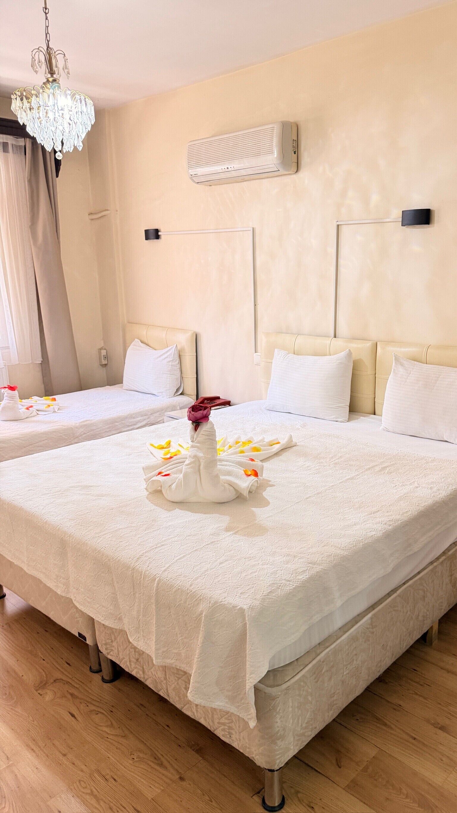A hotel room with two beds, a chandelier, an air conditioner, and a wall-mounted phone.