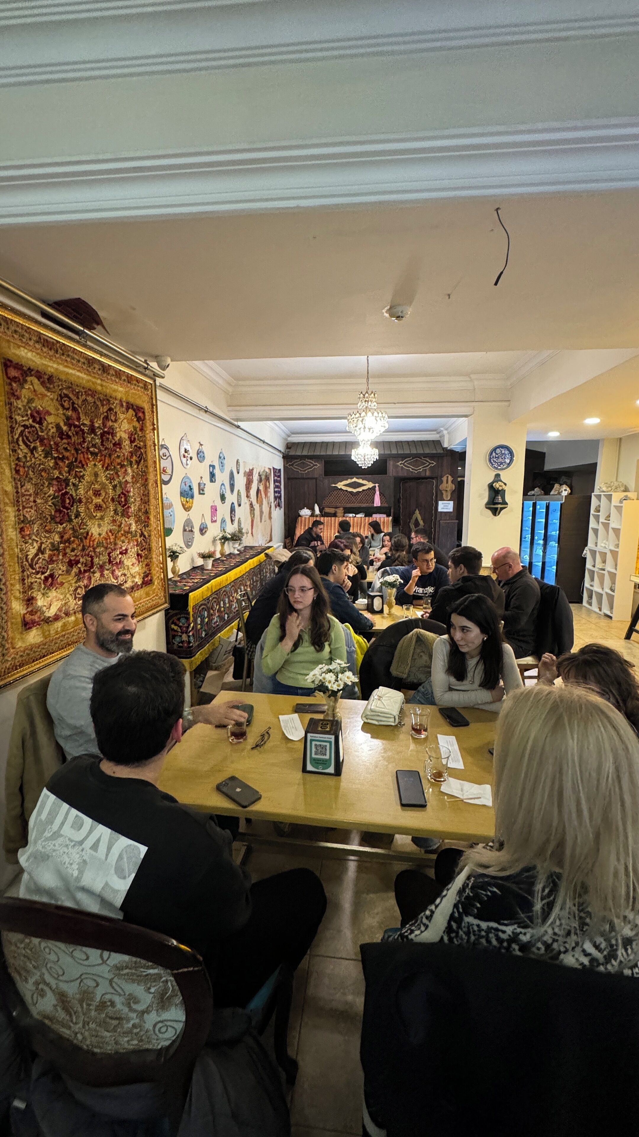 Un grupo de personas sentadas alrededor de una mesa de madera en una habitación con decoraciones ornamentales en las paredes y una lámpara de araña.