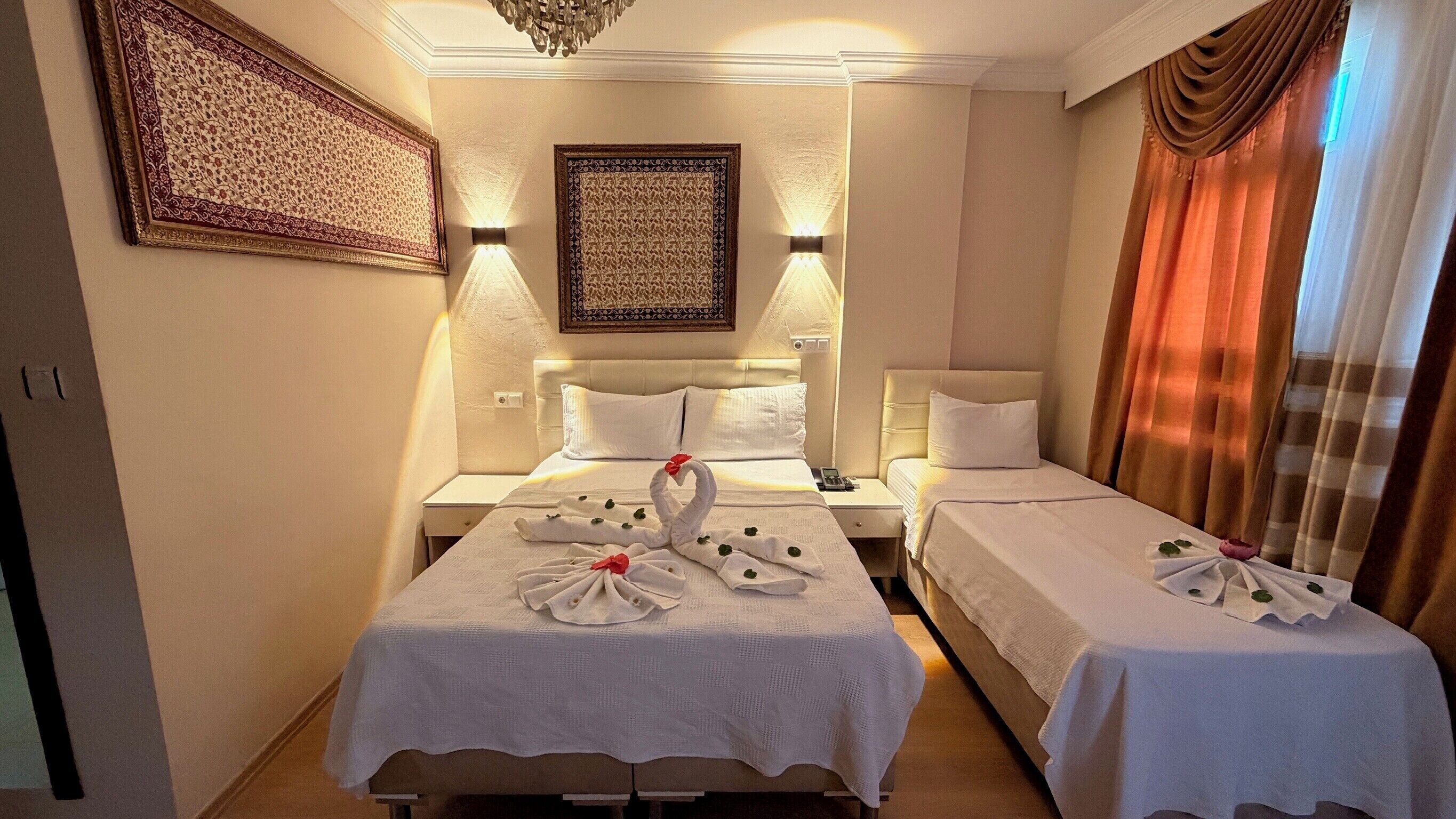 A hotel room with two beds, a chandelier, wall-mounted lamps, and a large decorative wall piece.