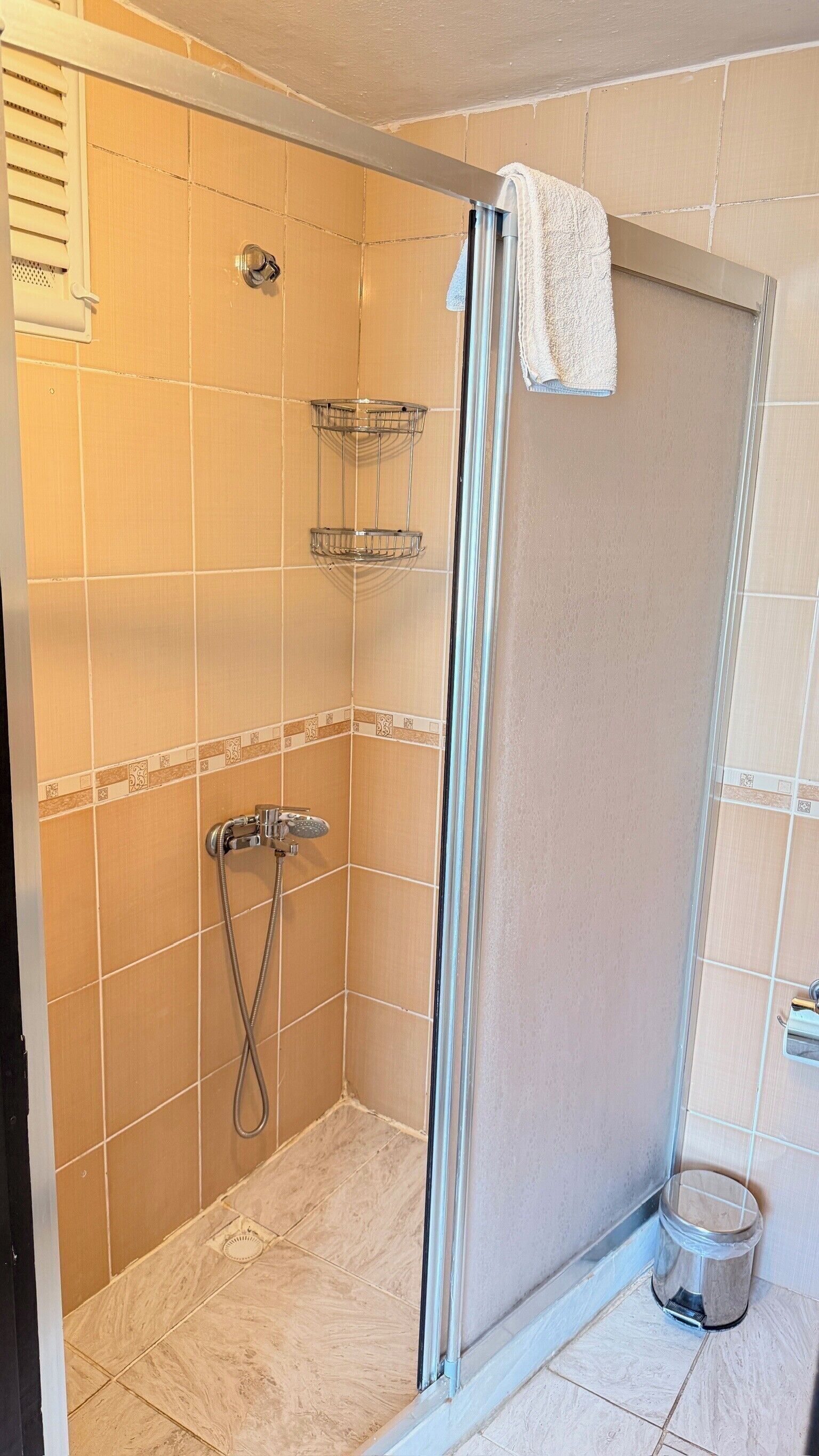 Une douche avec une porte en verre, une serviette accrochée à la porte et un pommeau de douche en métal.