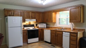 A kitchen with wooden cabinets, a refrigerator, stove, microwave, dishwasher, and a window providing natural light. - Comfortable lake living, pool access, 3 miles to marina (Monticello)
