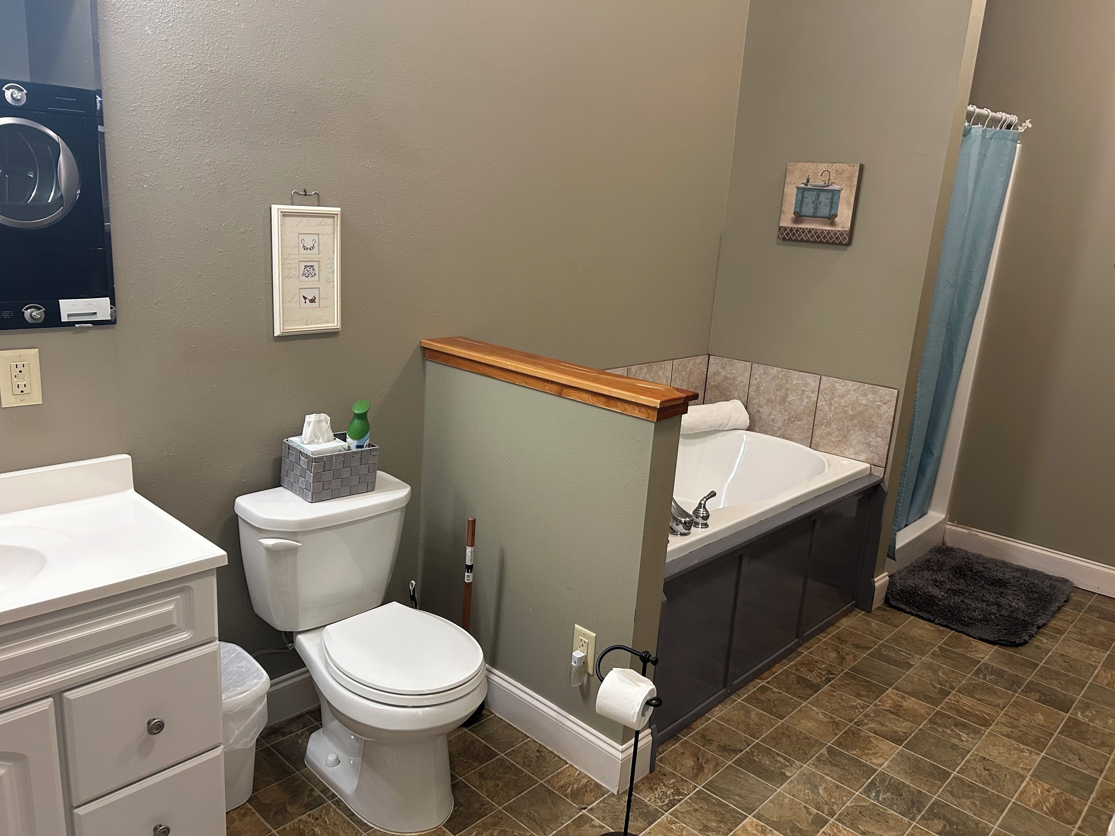 A bathroom with a toilet, sink, and bathtub. There is a towel rack, a picture on the wall, and a shower curtain.