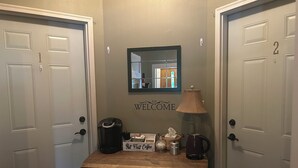 A hallway with two doors, a welcome sign, a coffee maker, a lamp, and a tissue box. - Room For Everyone! Book The Incredible Belltower Suites, Sleeps 16! (St Clair)