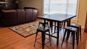A living room with a brown leather sofa, a wooden dining table with four stools, a patterned rug, and a large window with blinds. - Quiet, Comfortable Location! w/Double Garage
Easy access to WyoTech and UW (Laramie)