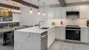 A modern kitchen with white cabinets, a marble island, and pendant lighting. - Top of the Village Leaf 501~Ski-in/out~HT~Pool~Grill~Parking (Snowmass Village)