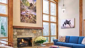 A cozy living room with a stone fireplace, large windows, and a blue sofa. - Top of the Village Leaf 501~Ski-in/out~HT~Pool~Grill~Parking (Snowmass Village)