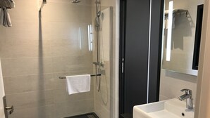 Ein modernes Badezimmer mit einer Glaskabine zur Dusche, einem weißen Waschbecken und einem großen Spiegel.