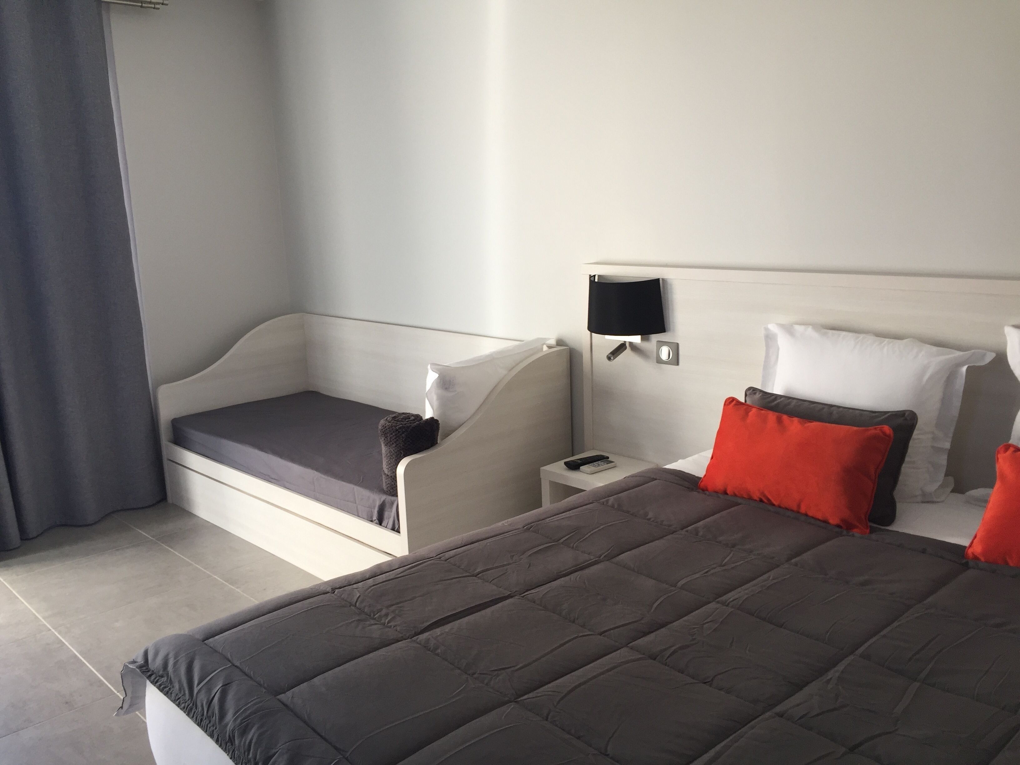 Una habitación de hotel con cama, mesita de noche, lámpara y ventana con cortinas.