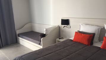 Una habitación de hotel con cama, mesita de noche, lámpara y ventana con cortinas.