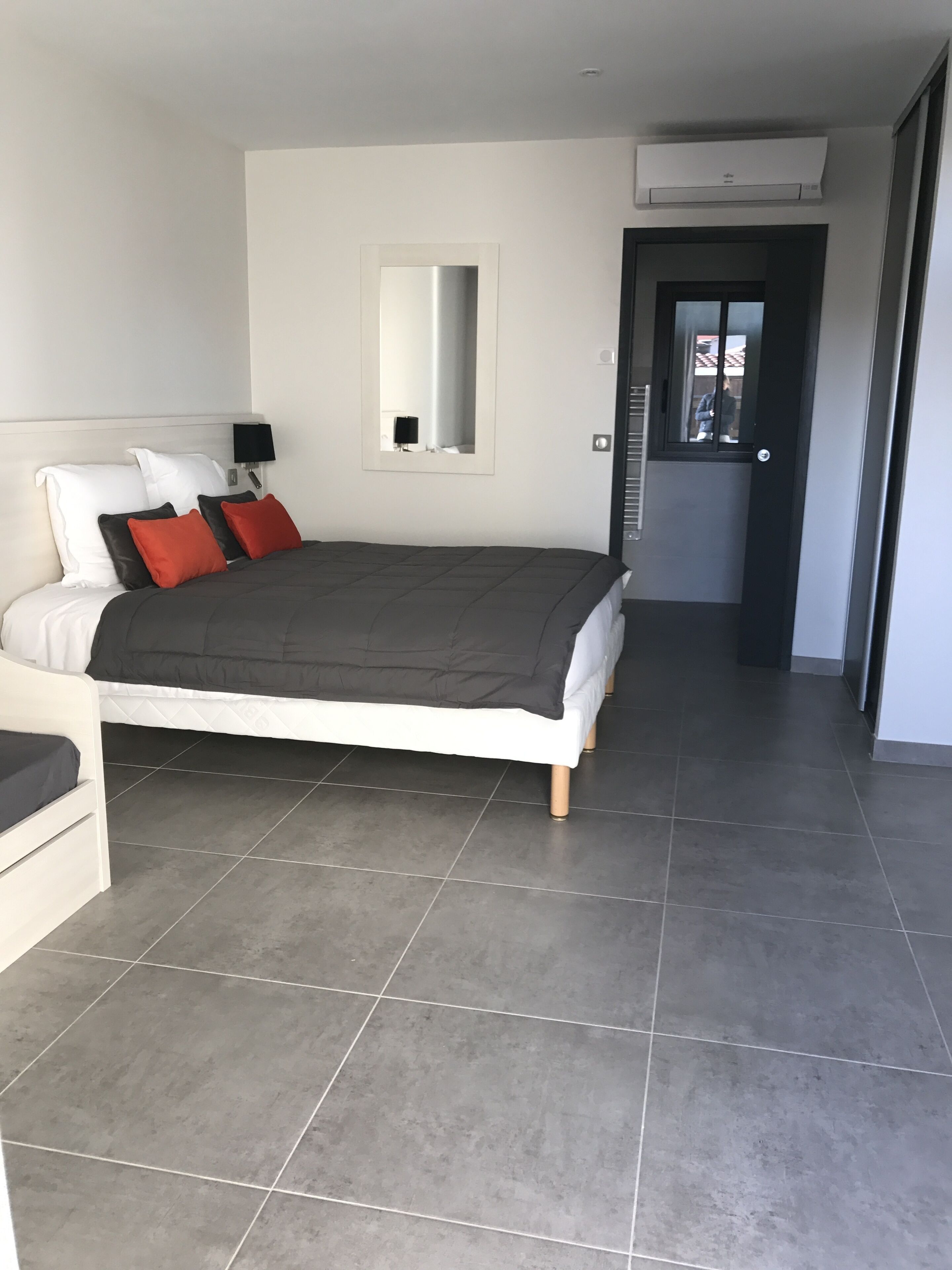 Ein modernes Schlafzimmer mit einem großen Bett, einem Nachttisch, einem Spiegel und einer Tür zu einem weiteren Raum.