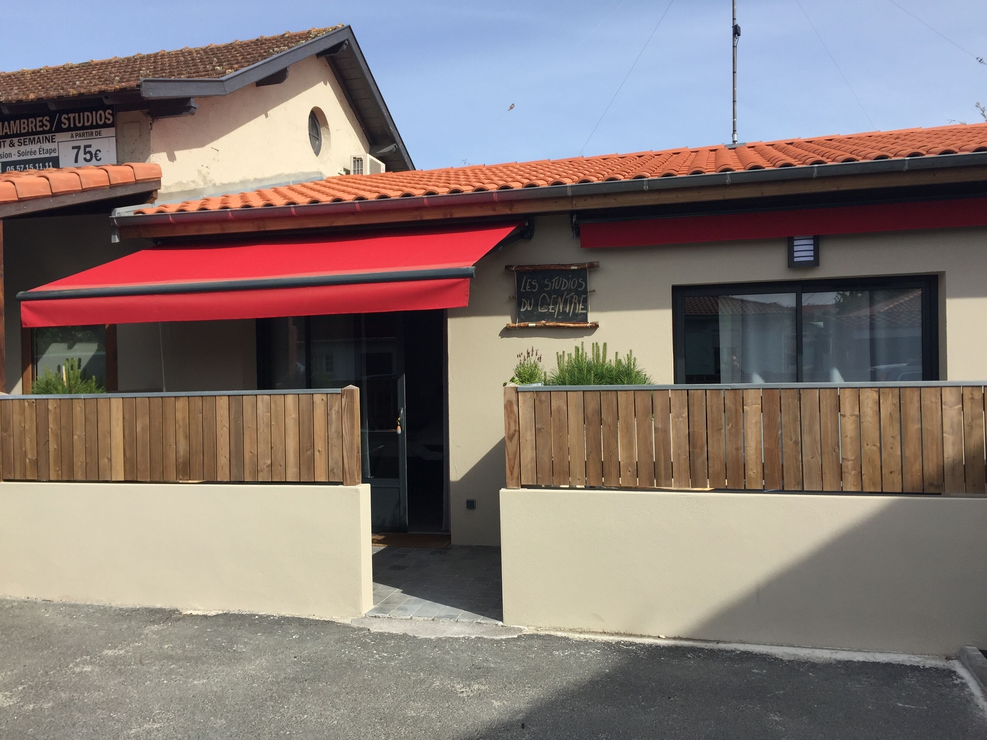 A building with a red awning, a wooden fence, and a sign that reads "Les Studios du Centre".