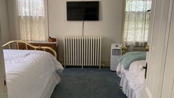 Une chambre avec deux lits, un radiateur, une télévision et une fenêtre avec des rideaux.
