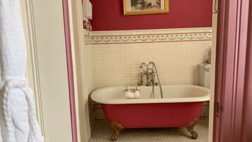 A bathroom with a clawfoot bathtub, a white toilet, and a red wall with a framed picture.