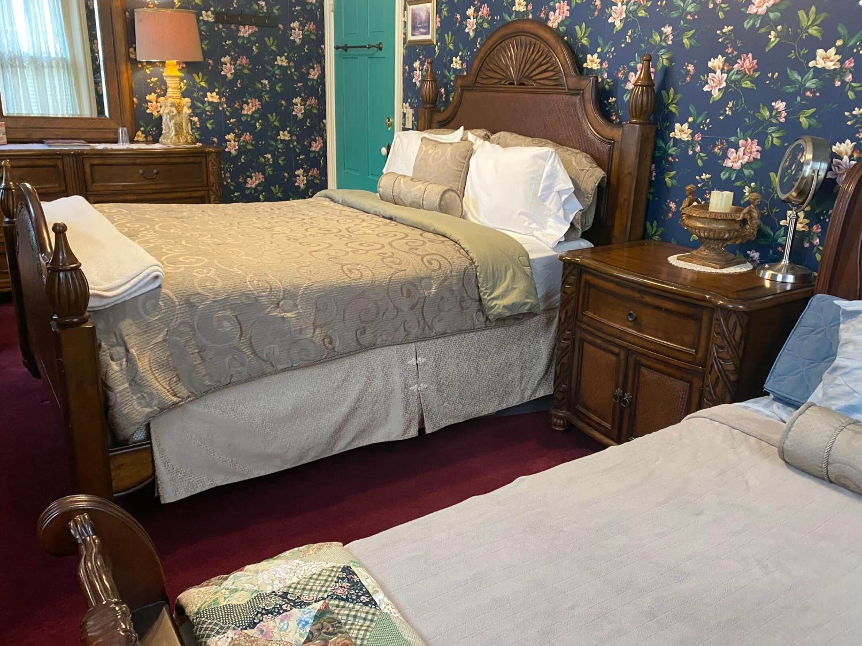 Une chambre avec deux lits, une tête de lit en bois, une table de chevet, une commode et un papier peint à motifs floraux.