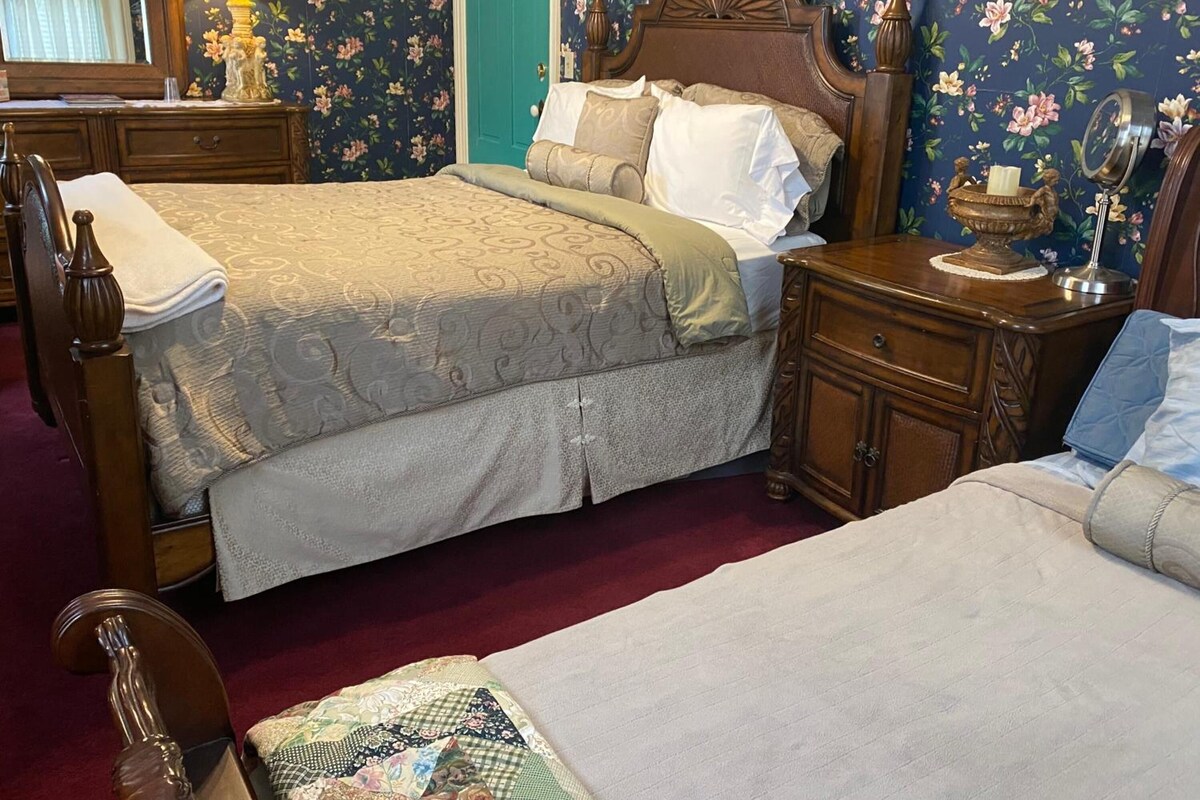 A bedroom with two beds, a wooden headboard, a nightstand, a dresser, and floral wallpaper.